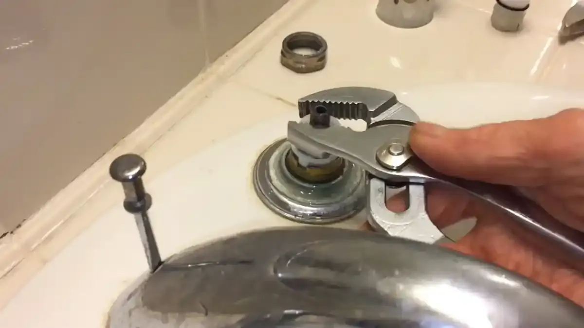 Hand using adjustable pliers on the stem of a bathtub faucet during a repair