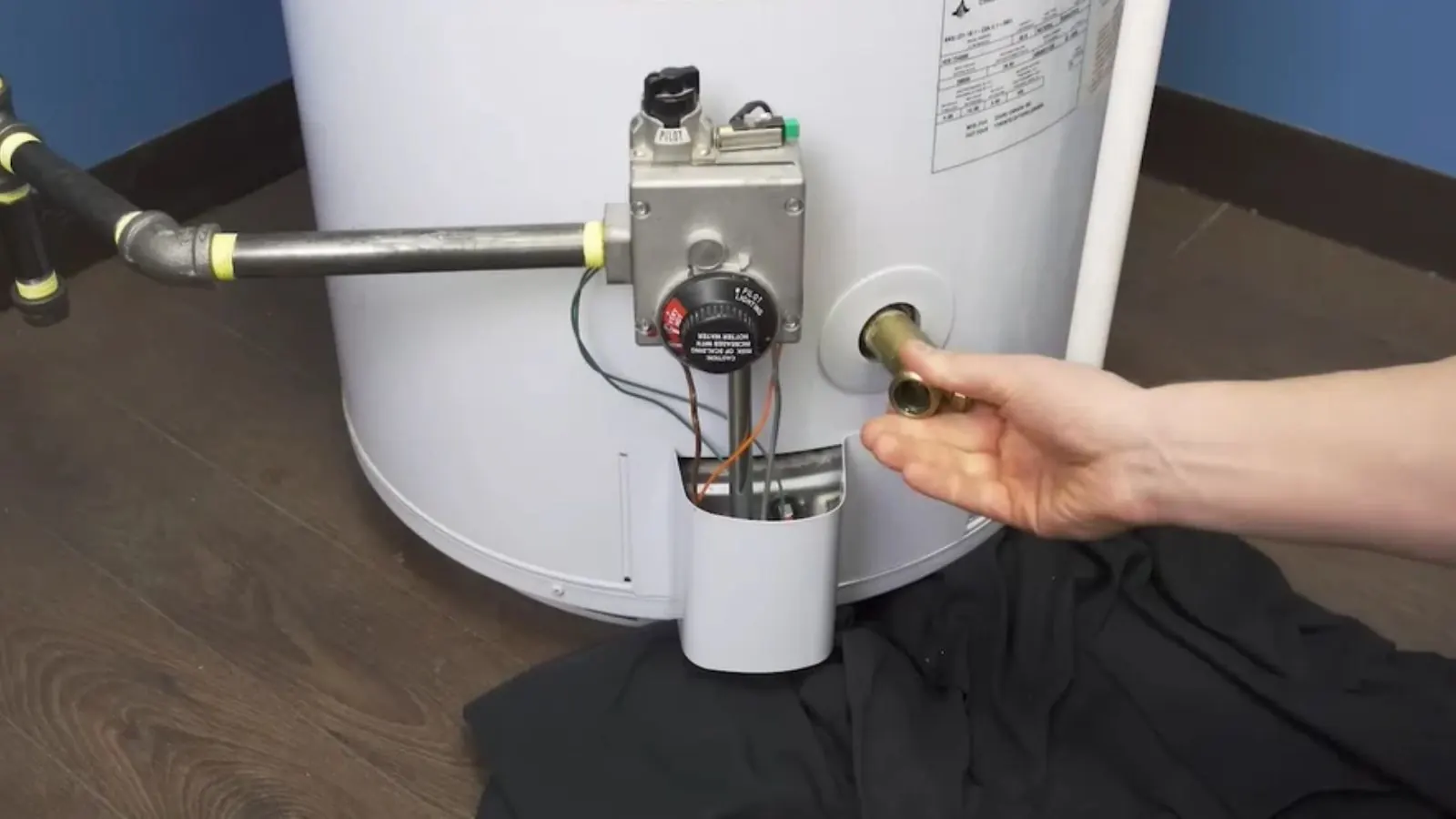 Hand holding the burner assembly of a gas water heater beside the igniter and gas valve